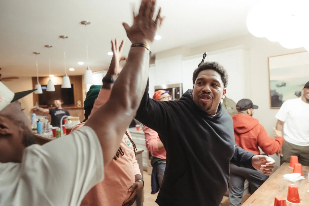 A man with both arms up mid-celebration in a crowded kitchen