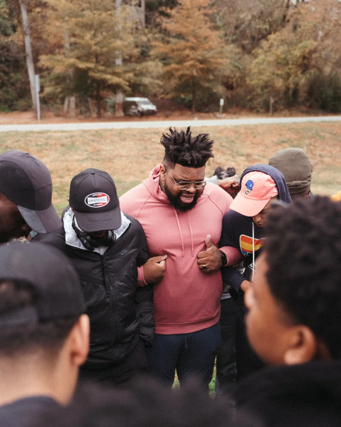 Men standing shoulder to shoulder in a close circle outdoors, hands joined in the middle