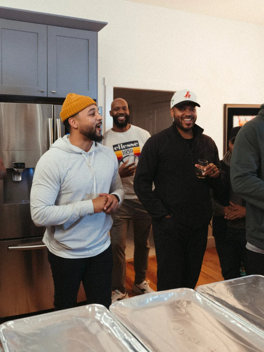 Men gathered at a kitchen counter over trays of food