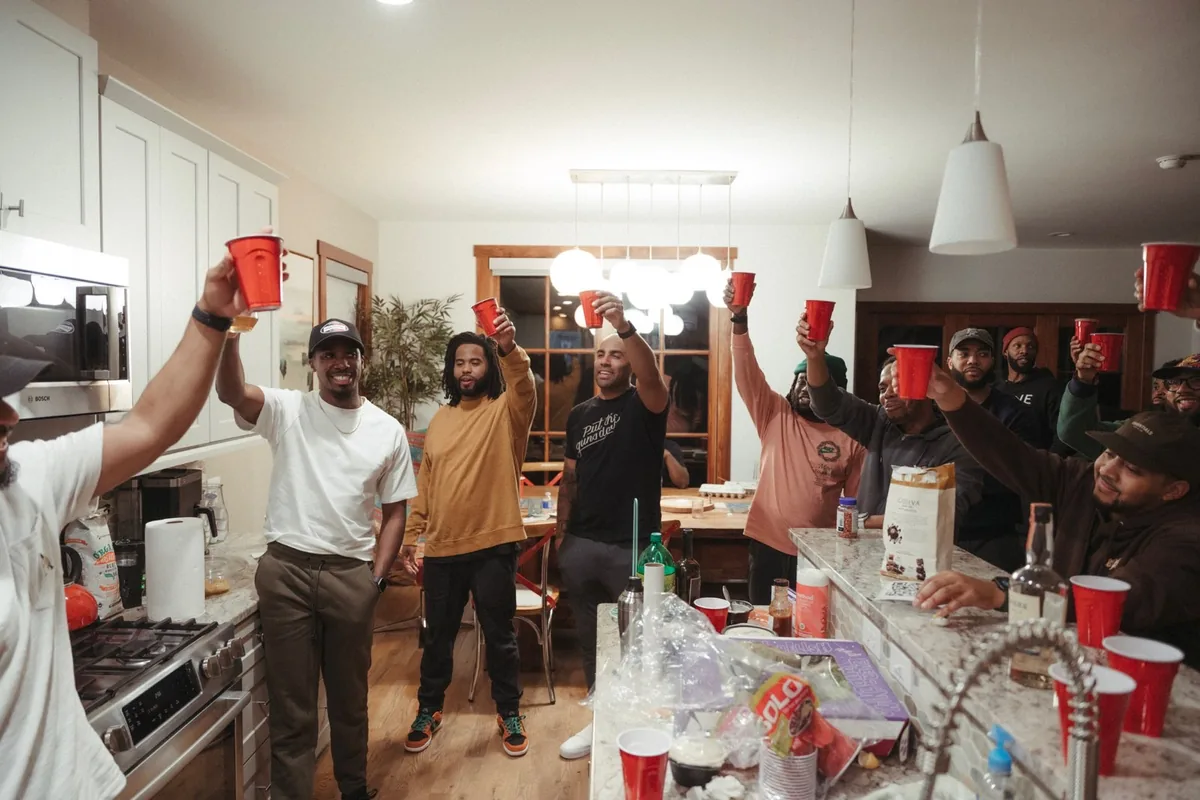Men raising cups together in a kitchen, mid-toast